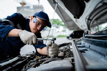 A mechanic is working on a car engine. The mechanic is wearing a blue shirt and a blue hat