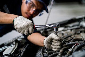 A mechanic is working on a car engine. The mechanic is wearing a blue shirt and a blue hat