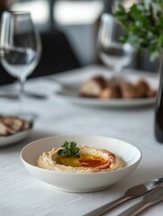 A bowl of hummus garnished with olive oil and parsley, set on a dining table.