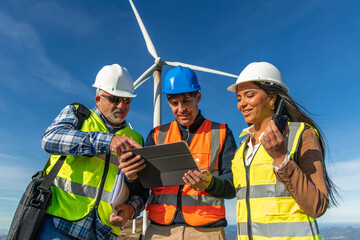 Three multiethnic Engineers using digital tablet, inspecting wind turbine for green energy