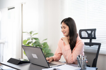 Fototapeta premium Confident businesswoman working on laptop at her workplace at modern office.Happy attractive asian business woman smiling working with laptop.