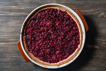 Delicious autumn pie on shortcrust pastry with red cranberries on a table. Cranberry cake with jam and sugar in a baking dish, rustic style, closeup, top view