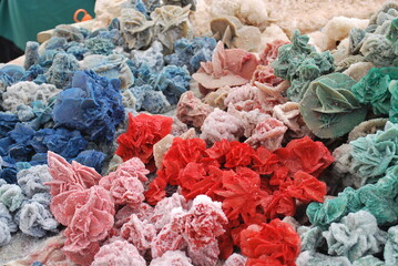 A vibrant display of colored desert rose mineral formations in shades of blue, red, green, and natural tones. These intricate crystal clusters highlight their unique textures and geological beauty, ar