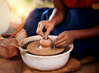 Fototapeta premium Close-up of hands shaping clay on a pottery wheel, creating a small pot. The scene depicts traditional craftsmanship and the artistry of pottery making.