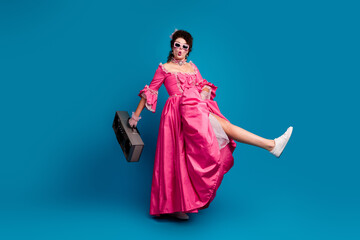 Vibrant young woman in a classic pink dress with vintage boombox and bold style on blue background