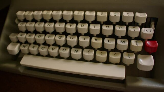 Top down view of a vintage typewriter keyboard with white keys featuring black text and symbols. The layout includes numbers, letters, and punctuation, red key and wide white space bar add contrast