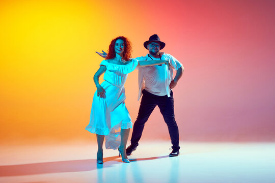 Salsa practice. Dancers, man and woman, refine their technique and fluidity in neon light against gradient orange background. Romantic vibe of dance. Concept of dance, performance, art, entertainment.