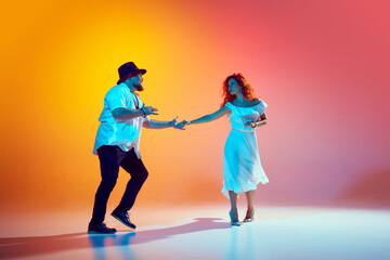 Salsa dancers practice with passion in neon light against gradient orange background, showing their...
