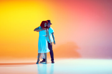 Energetic dancers practice with passion in neon light against gradient orange background, showing...
