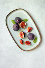 Plate with fresh ripe figs whole and slices with green leaves. Top view. Vertical photo