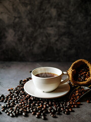 Americano coffee cup and roasted coffee beans falling in a burlap sackon gray background, Black coffee cup aromatic