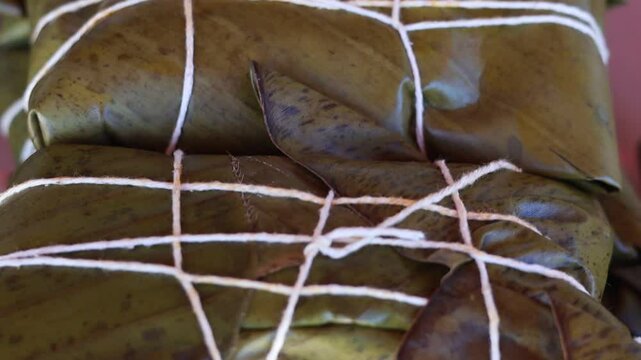  A close-up of a traditional Latin American dish wrapped in large leaves and tied with string. The image highlights the unique presentation and cultural significance of this culinary tradition.