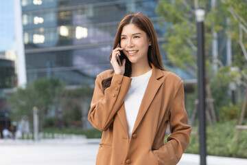 Female Worker using phone. A confident Asian businesswoman engages in digital remote work while enjoying the urban landscape.