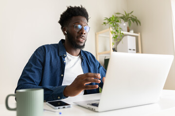 African american man looking at laptop screen during video call at home office.