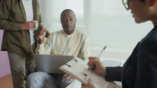 Tilt up shot of three diverse colleagues collaborating on project discussion while meeting at modern inclusive office