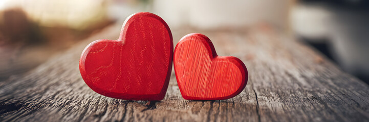 Two red wooden hearts on a rustic wooden surface, symbolizing love and connection in a warm atmosphere