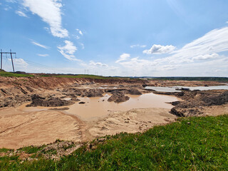 Large excavation area features muddy water pools and rocky terrain under a bright sky in a rural setting