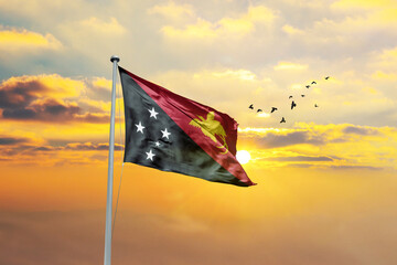 Waving flag of Papua New Guinea against sunset or sunrise. Papua New Guinea flag for Republic Day...