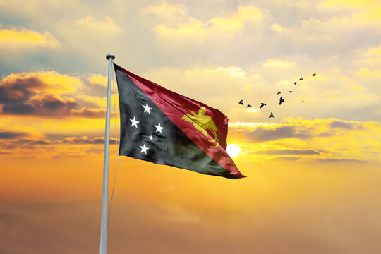 Waving flag of Papua New Guinea against sunset or sunrise. Papua New Guinea flag for Republic Day and Independence Day. - Powered by Adobe
