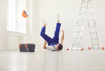 Young construction male worker in uniform fallen dawn from ladder indoors. Injured handyman lying on the floor after accident on his workplace. Injury, insurance and safety concept. © Studio Romantic