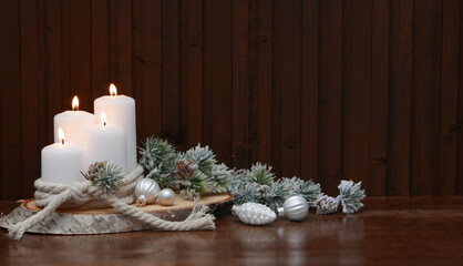 Weihnachtshintergrund: Dekoration mit weissen Kerzen und Weihnachtskugeln auf einer Baumscheibe vor einem rustikalem Holzhintergrund mit Textfreiraum.