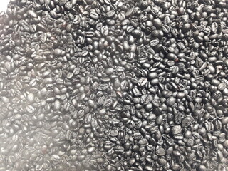 Freshly roasted coffee beans emit smoke inside, black coffee beans background. natural manual roast.