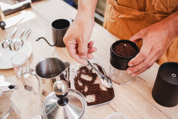 Barista is grinding coffee beans with manual stainless steel grinder to make black coffee machine, brewing equipment or coffee drip set Dripper on a wooden table In the kitchen at home in the morning.