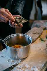 A person is cooking food in a silver pot. The pot is filled with a variety of ingredients, including some spices. The person is using a spoon to add more spices to the pot