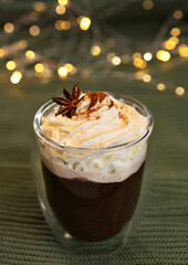 Coffee with whipped cream and spices in a glass with double walls on a bokeh background.