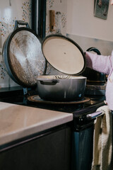 A woman is cooking in a kitchen with a pot on the stove. The pot is open and the woman is standing next to it