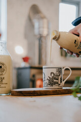 A person is pouring milk into a white mug. The milk is from a bottle that says 