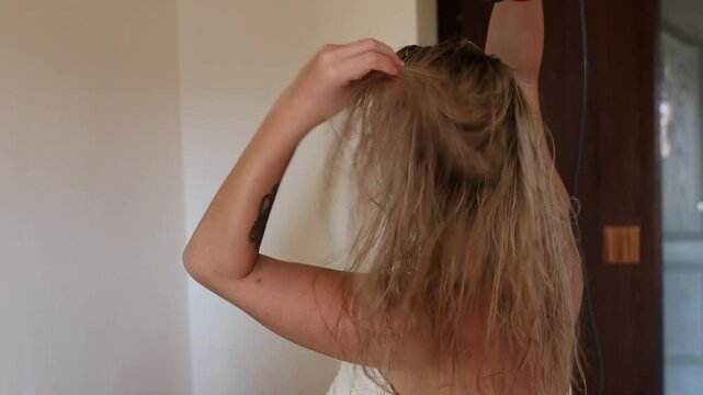 Young woman drying her hair with a styler, a hair dryer at home