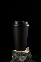 Black coffee cup stands on a textured rock surface against a dark background