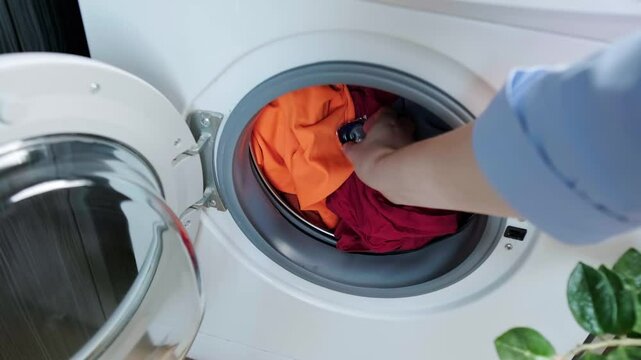 Woman places a laundry capsule into the washing machine drum and closes the door, using detergent pods with fabric softener for washing.