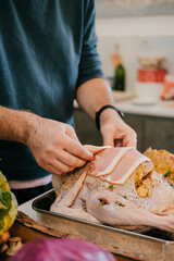 A man is preparing a turkey with bacon on it. He is using a knife to cut the bacon and is placing it on the turkey