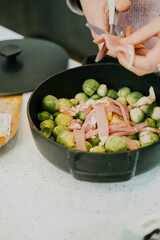 A person is preparing a meal with a black pot and a white plate. The meal consists of broccoli and ham