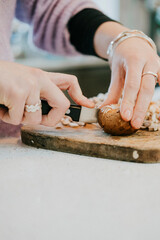 A woman is cutting a potato on a wooden cutting board. She is wearing a ring and a bracelet