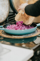 A person is cooking food in a blue pan. The food is purple and he is cabbage