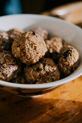 A bowl of small, round food items sits on a wooden table. The food items are brown and appear to be some type of baked goods. The bowl is filled to the brim