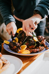 A person is cutting a roasted chicken with a knife and a fork. The chicken is served on a blue plate with orange slices