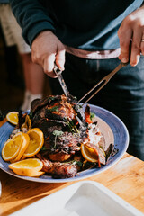 A person is cutting a large piece of meat on a blue plate with oranges on it. The plate is placed on a wooden table