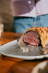 A piece of meat is cut in half and is on a plate. The plate is on a wooden table