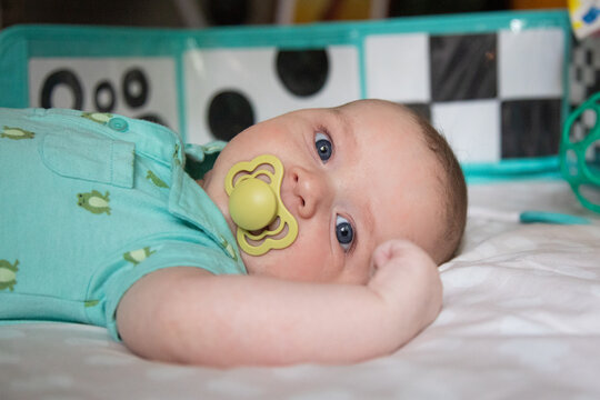 Close-up of a baby boy with a pacifier lying in a cot