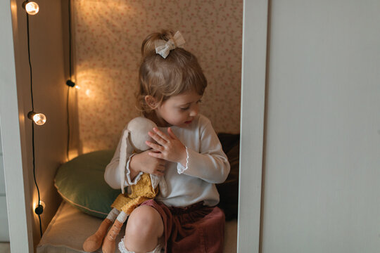 Close-up of a young girl cuddling a stuffed toy sitting in a den decorated with garlands of light bulbs