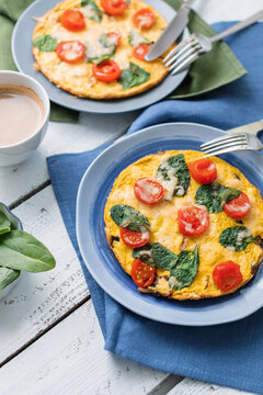 Close-up of two cheese, cherry tomato and spinach omelettes with a cappuccino on a wooden table