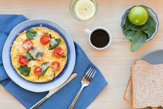 Overhead view of a cheese, cherry tomato and spinach omelette with brown bread, black coffee and lemon water