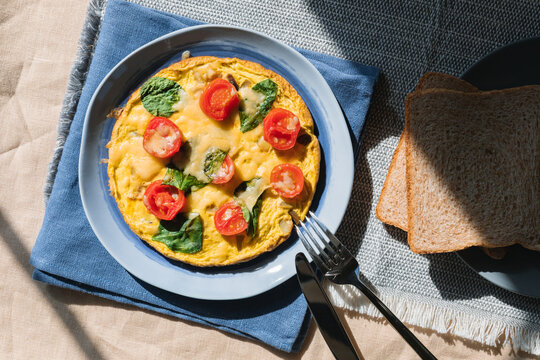 Overhead view of a cheese, cherry tomato and spinach omelette with brown bread on a table
