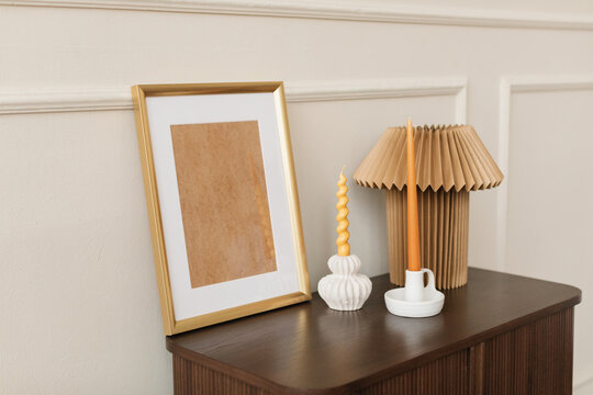 Empty wooden picture frame with two candlesticks and a lamp on a chest in a stylish living room