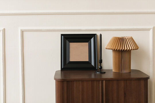 Empty wooden picture frame with a candle and lamp on a chest in a stylish living room
