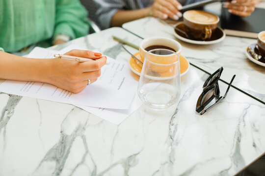 Two young women discussing work processes, signing documents and drinking coffee at a cafe